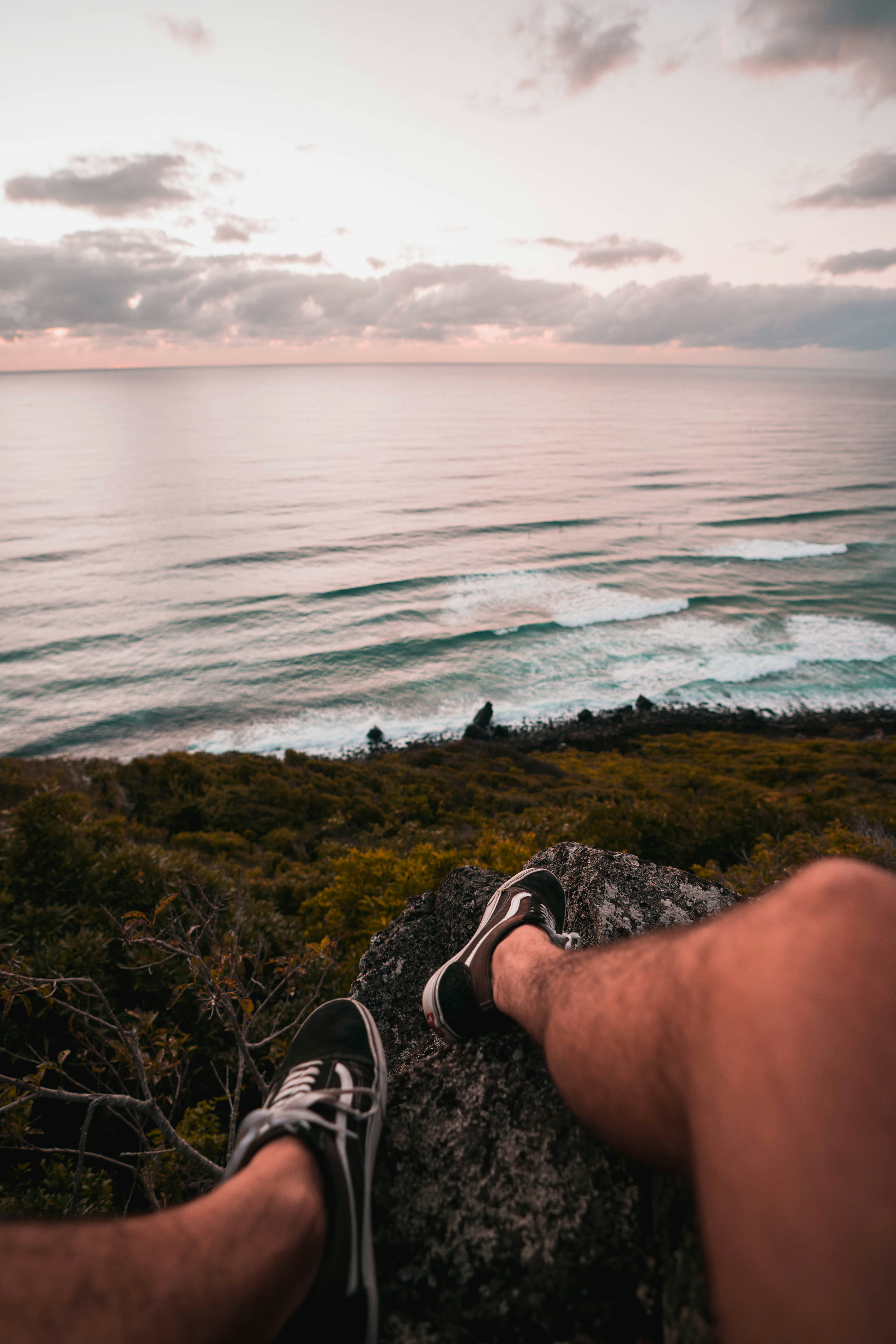 person in black and white sneakers sitting on rock near body of water during daytime